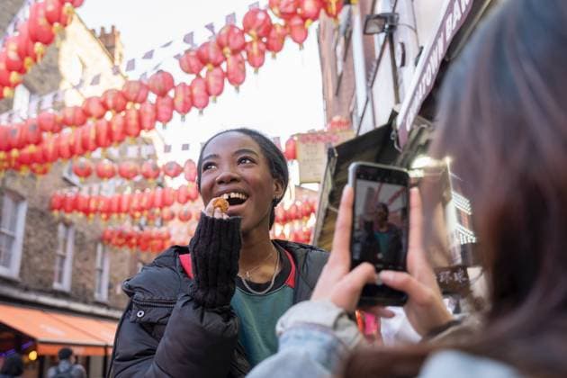 Young woman taking picture of friend eating taiyaki in Chinatown model released Copyright: xCulturaxCreativex