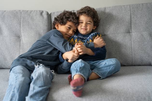Brothers (2-3, 6-7) hugging on sofa at home model released Copyright: xCulturaxCreativex