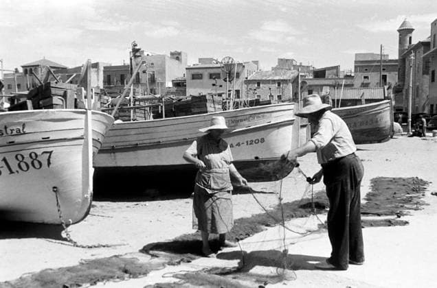Zu Besuch in L Escala Eine Frau und ein Mann in breitkrempigen Strohhüten breiten Fischernetze am Strand von L Escala aus, auf dem etliche Fischerboote liegen, den Hinterrgund säumt die ortstypische Architektur, Costa Brava 1957. A woman and a man in wide-brimmed straw hats spread out fishing nets on the beach at L Escala, where a number of fishing boats are moored, with typical local architecture lining the background, Costa Brava 1957., L Escala Katalonien Spanien Copyright: ErichxAndres EAN_6210155