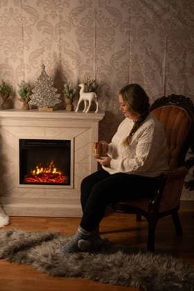 Woman sitting by a fireplace with a holiday decor, holding a mug Waunakee, Wisconsin, United States R_SUKG2408058F-1462338-01 ,model released, Symbolfoto