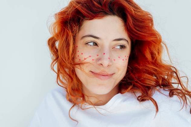 Creative Highlights Symbolbilder Smiling redhead woman with heart stickers on face against white background model released, Symbolfoto, PGF01852