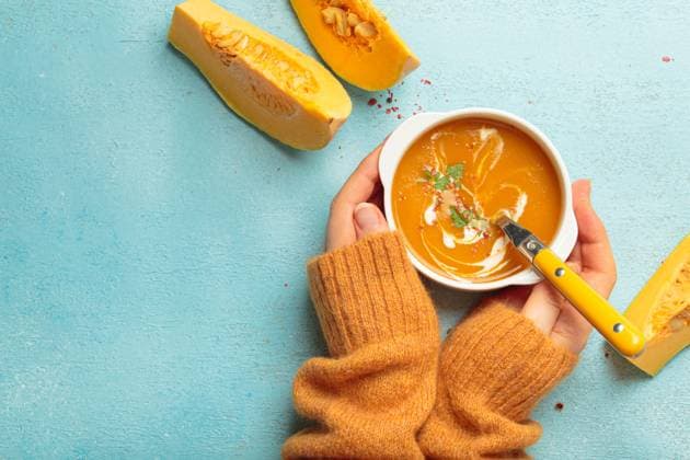 Woman holding spoon eating butternut squash soup with cream on blue background top view Woman in an orange sweater enjoys a bowl of butternut squash soup with cream and spices on a cozy blue background, perfect for autumn comfort Copyright: xZoonar.com OlenaxYeromenkox 22067096