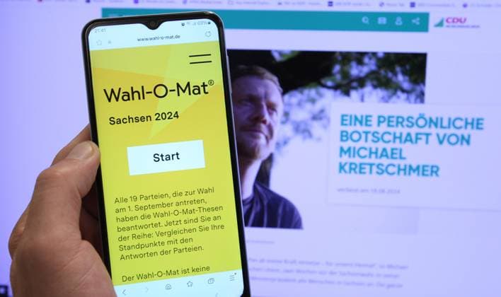 Auf einem Smartphone wurde der Wahl-O-Mat für die Landtagswahl in Sachsen geöffnet. Dahinter ist auf einem Bildschirm der Spitzenkandidat der CDU für die Wahl, Michael Kretschmer, zu sehen. Schnelsen Hamburg *** The Wahl O Mat for the state election in Saxony was opened on a smartphone Behind it, the CDUs top candidate for the election, Michael Kretschmer, can be seen on a screen Schnelsen Hamburg