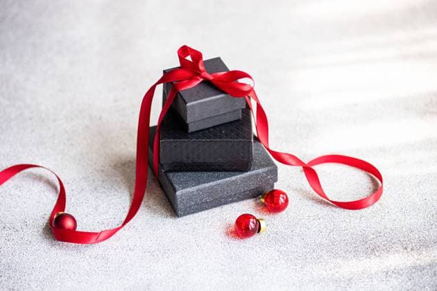 Top view of black textured gift boxes adorned with a silky red ribbon, complemented by tiny red baubles, arranged on a textured light background. Model Released AnnaBogush_ID23676_687469_012 Copyright: xAnnaxBogushx