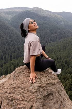 Creative Highlights Symbolbilder A young woman with eyes closed, smiling in contentment, sits atop a rocky peak against a lush mountain backdrop. She™s wearing a loose T-shirt, leggings, and sunglasses, exuding a sense of peace and achievement in the serene forest setting. Model Released EduardoGavira_ID23247_676238_005 Copyright: xEduardoxGavirax RECORD DATE NOT STATED