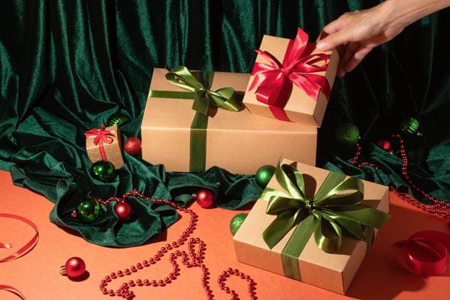 A hand adds a vibrant red bow to a wrapped gift, set against a backdrop of lush green velvet and holiday ornaments The scene captures the spirit of festive gift-giving Model Released OlgaVila_ID23685_687641_010 Copyright: xOlgaxVilax