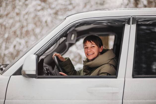 Fröhliche Frau lächelt und schaut in die Kamera, während sie ein modernes Fahrzeug auf einem unscharfen Hintergrund einer verschneiten Landschaft fährt Cheerful female smiling and looking at camera while driving modern vehicle on blurred background of snowy countryside Copyright: imageBROKER DashaxPetrenko ibxiqx09193876.jpg ,model released, Symbolfoto ,property released