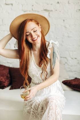 Creative Highlights Symbolbilder Glückliche junge Frau in Boho Kleid und Hut genießt Wein mit Lächeln, während sie auf einer Bank vor einer weißen Backsteinmauer sitzt Happy young female in boho dress and hat enjoying wine with smile while sitting on bench against white brick wall Copyright: imageBROKER DashaxPetrenko ibxiqx09195774.jpg ,model released, Symbolfoto ,property released