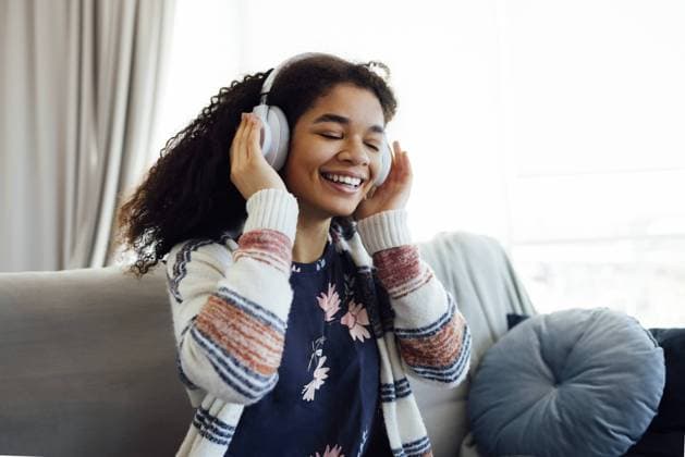 Afrikanische Millennial Frau im orangefarbenen Pullover, die weiße drahtlose Kopfhörer trägt, Musik hört, sich ausruht und auf der Couch im Wohnzimmer liegt. Mädchen verbringen faul Wochenende zu Hause African millennial woman in orange sweater wearing white wireless headphones, listening music, resting and lying on couch in living room. Girl spend lazy weekend at home Copyright: imageBROKER DashaxPetrenko ibxiqx09199434.jpg ,model released, Symbolfoto ,property released