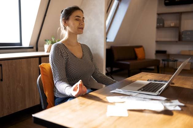 Stressabbau während der freiberuflichen Arbeit. Brünette Frau Freiberufler sitzt in Lotuspose und meditiert mit den Händen in Mudra Geste auf dem Stuhl vor dem offenen Laptop auf dem Tisch, von zu Hause aus arbeiten Stress relief during freelance work. Brunette woman freelancer sitting in lotus pose and meditating with hands in mudra gesture on chair in front of open laptop on table, working from home Copyright: imageBROKER DashaxPetrenko ibxiqx09201393.jpg ,model released, Symbolfoto ,property released