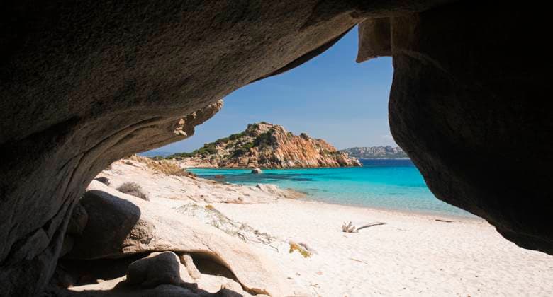 View through cave entrance across the clear turquoise waters of Cala Corsara to the pink granite headland of Punta Rossa Corsara, Spargi Island, La Maddalena Archipelago National Park, Sassari, Sardinia, Italy, Mediterranean, Europe Copyright: DavidxTomlinson 1310-385 RECORD DATE NOT STATED