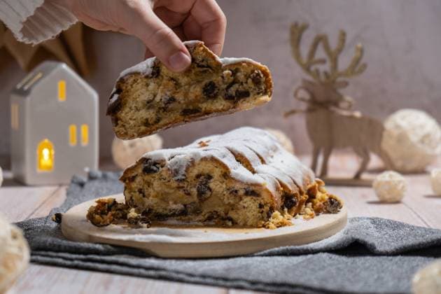 Female hand taking slice of Christmas Stollen in Christmas lights and decoration. Traditional sweet fruit loaf with icing sugar festive pastry dessert. Holiday baking food Female hand taking slice of Christmas Stollen in Christmas lights and decoration. Traditional sweet fruit loaf with icing sugar festive pastry dessert. Holiday baking food concept. Copyright: xZoonar.com AnastasiiaxYanishevskax 22151901