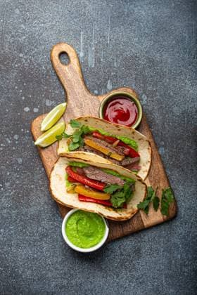 IMAGO Creative, Food, Fajita Traditionelles mexikanisches Gericht Rindfleisch Fajitas Tacos serviert auf hölzernen Schneidebrett mit Tomaten-Salsa und Guacamole auf rustikalen Stein Hintergrund von oben, American Mexican Food Traditional Mexican dish Beef fajitas tacos served on wooden cutting board with tomato salsa and guacamole on rustic stone background from above, American Mexican food Copyright: imageBROKER OlenaxYeromenko ibxiqx08607073.jpg