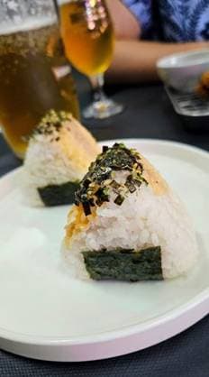 IMAGO Creative, Food, Japan, Onigiri Close-up of two onigiri rice balls with seaweed and seasoning on a white plate, with beverages in the background. 25793096 RECORD DATE NOT STATED