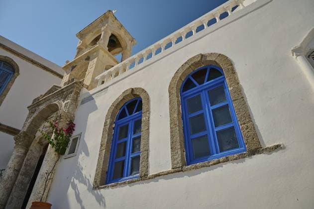 IMAGO Creative, Herbst, Reiseziel, Dodekanes, Griechische Inseln Weißes Gebäude mit blauen Fenstern und Steinbögen unter einem blauen Himmel und einem Kirchturm im Hintergrund, Platia und Kirche Issodia Theotokou, Nikia, Nisyros, Dodekanes, Griechische Inseln, Griechenland, Europa White building with blue windows and stone arches under a blue sky and a church tower in the background, Platia and church Issodia Theotokou, Nikia, Nisyros, Dodecanese, Greek Islands, Greece, Europe Copyright: imageBROKER RalfxAdler ibxraa11255359.jpg