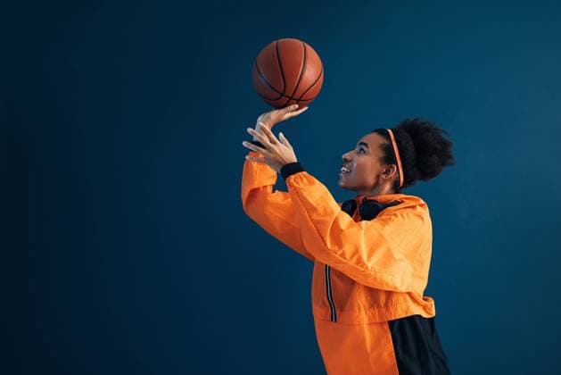 Creative Highlights Symbolfotos Side view of smiling basketball player in orange fitness attire practicing throwing over blue background Side view of smiling basketball player in orange fitness attire practicing throwing over blue background Copyright: xxArtemxVarnitsinx