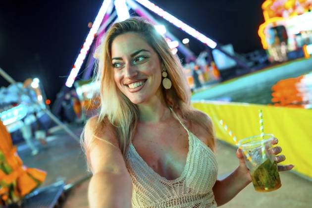 Creative Highlights Symbolfotos Blonde lächelnde Frau, die ein Selfie macht, während sie einen Cocktail auf einer Messe in der Nacht trinkt Blonde smiling woman taking selfie while drinking cocktail at fair at night Copyright: imageBROKER UnaixHuizi ibxuhu10986224.jpg ,model released, Symbolfoto ,property released