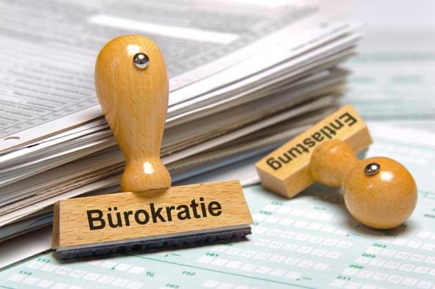 Akten und Bürokratieentlastung Ein Holzstempel ist beschriftet mit dem Aufdruck Bürokratieentlastung und lehnt an einem Stapel Formulare *** Files and red tape relief A wooden stamp is labeled with the words red tape relief and leans against a stack of forms