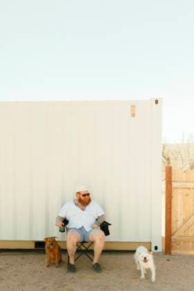 Creative Highlights Symbolfotos Man in a chair with a small dog beside a white container in the deser Joshua Tree, California, United States CR_QCYJ240904-1531027-01 ,model released, Symbolfoto