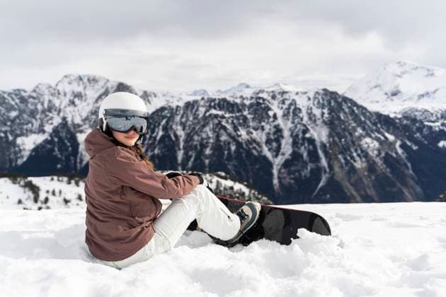Teenage girl wearing helmet and sitting with ski on snow in front of mountains model released, Symbolfoto, NJAF01363