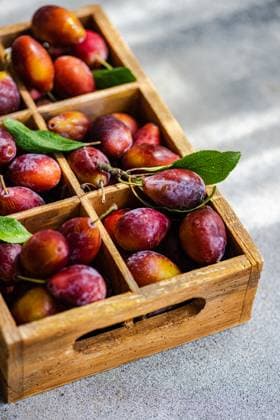IMAGO Creative, Jahreszeit Sommer, Food, Pflaume From above organic ripe plums freshly picked from the orchard, neatly arranged in a rustic wooden crate. The vibrant colors of the plums range from deep purples to rich reds, with fresh green leaves adding a touch of natural beauty. Model Released AnnaBogush_ID23878_692869_003 Copyright: xAnnaxBogushx