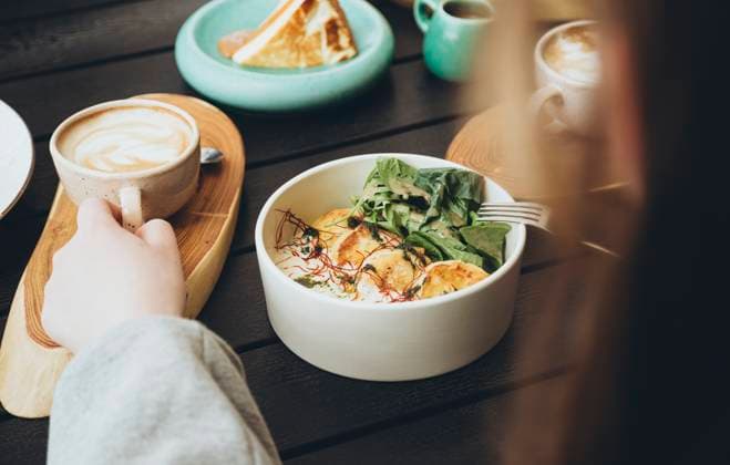 Cropped unrecognizable person enjoying a morning meal at a cafe, featuring a cup of coffee and a bowl with grilled halloumi and arugula, and a side of toast. Model Released HannaYakimenko_ID24020_696571_025 Copyright: xHannaxYakimenkox