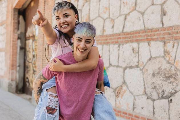 Creative Highlights Symbolfotos A lesbian couple happily engages, with one woman carrying the other on her back, pointing towards something exciting Their smiles and alternative style, including tattoos and colorful hair, highlight the diversity within the LGBTQIA+ community Model Released JoseCarlosIchiro_ID23627_686150_041 Copyright: xJosexCarlosxIchirox