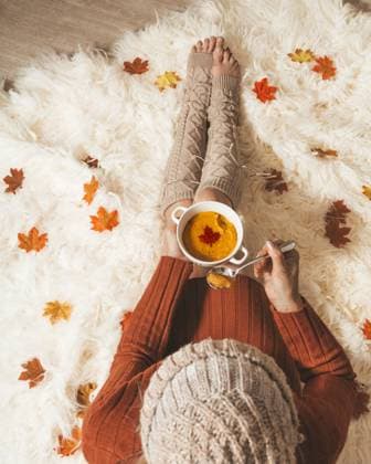Woman holds a bowl of spiced pumpkin soup sitting on cozy rug Woman on a fluffy cozy rug holds a bowl of spiced pumpkin soup in the fall autumn season. Overhead perspective with scattered maple leaves ,model released, Symbolfoto Copyright: xZoonar.com Leah-AnnexThompsonx 15611923 ,model released, Symbolfoto ,property released