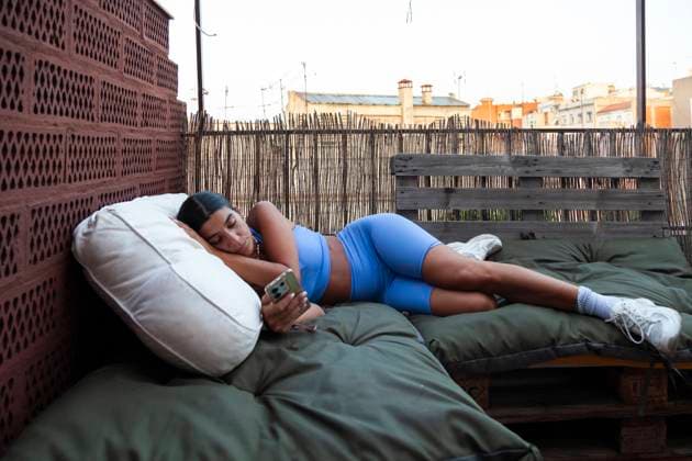 Creative Highlights Symbolfotos Woman lies comfortably on outdoor bed while operating her smartphone at sunrise in Barcelona, looking at the screen Model Released Almuzambrana_ID23844_692095_008 Copyright: xAlmuzambranax