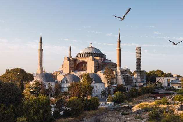Warm evening light bathes the historic Hagia Sophia in Istanbul, with soaring birds enhancing the tranquil scene. This landmark showcases Byzantine architecture surrounded by smaller structures and lush greenery. Model Released DavidMunoz_ID24078_697534_021 Copyright: xDavidxMunozx
