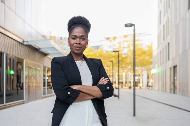 Creative Highlights Symbolfotos Confident African American woman in a smart black blazer and white dress stands with arms crossed, looking at the camera, positioned in a modern business district setting. Model Released DavidMunoz_ID24206_701900_068 Copyright: xDavidxMunozx