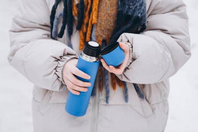 Cropped anonymous teen girl in a warm coat enjoys a winter stroll while holding a vibrant blue thermos. Close-up of hands pouring a drink, fostering a cozy, seasonal feel. Model Released HannaYakimenko_ID24348_706101_002 Copyright: xHannaxYakimenkox
