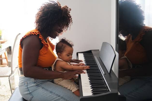 A heartwarming image of an African mother helping her baby girl play the piano Both share a moment of joy and learning in a brightly lit room Model Released HaruUraraStudio_ID24141_699425_034 Copyright: xHaruxUraraxStudiox RECORD DATE NOT STATED