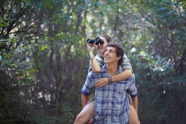 Man, woman and piggyback outdoor with binocular for travel, adventure or sightseeing in nature with happiness. Couple, people and tourist hiking in woods or forest for experience, holiday or vacation. model released property released Copyright: xwww.peopleimages.comx