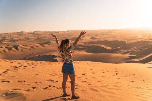 Creative Highlights Symbolfotos A woman in her 20s stands on a vast desert dune, arms raised, under a clear sky, embracing the serene landscape. 26230602 ,model released, Symbolfoto RECORD DATE NOT STATED