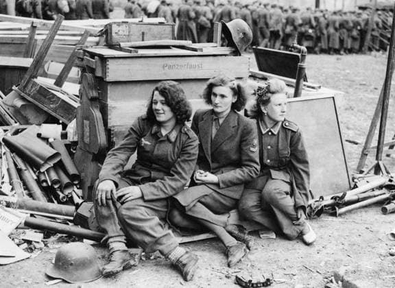 Orig. caption... GERMAN WOMEN ARMY PRISONERS Great masses of German prisoners are continually arriving at the cages set up at a former Nazi Military Academy in the 7th Army area. Amongst them are also women prisoners: truck drivers, Luftwaffe personnel (similar to W.A.A.F.s) cooks from military camps etc. These women are segregated from the men and are quartered in the buildings of the Academy, in rooms formerly used for military lectures. Photo shows: Sitting on German ammunition boxes with wrecked machine guns and equipment lying in the mud, three German women army prisoners await transport. The girl on the left is aged 18 and comes from Frankfurt-on-Main. She was in the Signal Corps. The center girl is 21, from Bauen, and served with the  Copyright: xXxXxXx FEMALE PRISONERS OF WAR