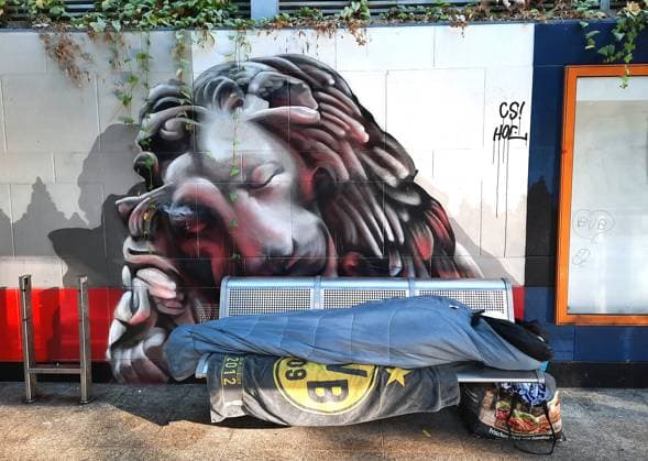 A homeless man sleeps under the mural of a sleeping lion on a bench at the S-Bahn station Möllerbrücke in Dortmund, 15 10 2024