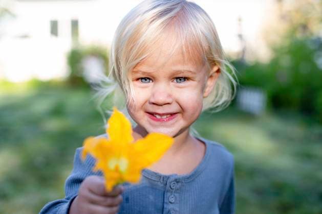 Creative Highlights Symbolfotos Smiling toddler holding a yellow flower outdoors with a house in the background. arah00727 Copyright: xConnectxImagesx ,model released