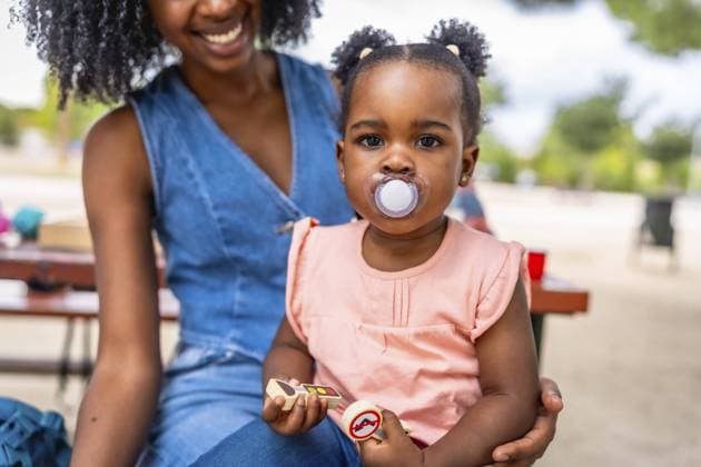 Creative Highlights Symbolfotos Niedliches afrikanisches Mädchen mit Schnuller auf Mamas Schoß im Park sitzend Cute african girl with pacifier sitting on mom s lap in the park Copyright: imageBROKER UnaixHuizi ibxuhu11544291.jpg ,model released, Symbolfoto ,property released