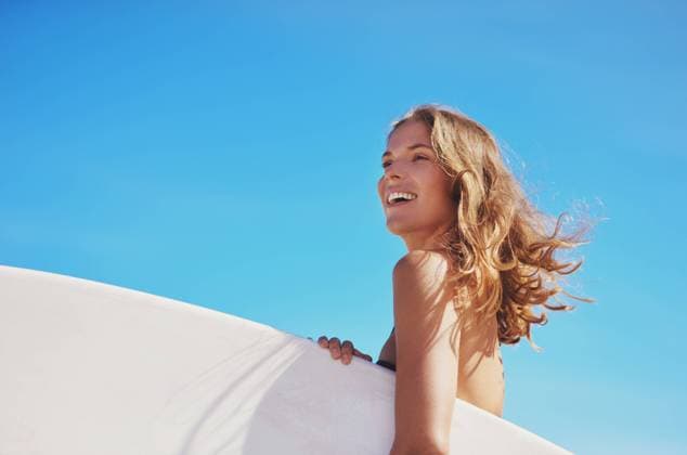 Creative Highlights Symbolfotos Girl, laughing and board for surfing in outdoor, workout and blue sky for water sports competition. Female person, mockup space and travel to ocean for waves, calm and athlete for exercise in nature. model released property released Copyright: xwww.peopleimages.comx