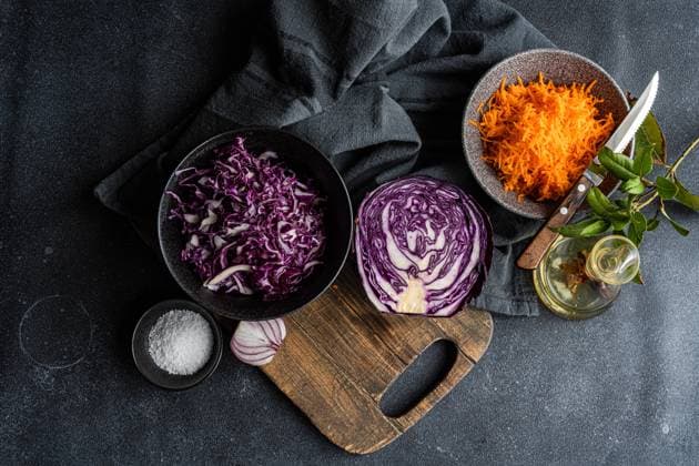 A dark surface hosts a variety of vibrant salad ingredients including shredded red cabbage, grated carrot, sliced red onion, olive oil, and a bowl of sea salt, ready for a healthy meal preparation Model Released AnnaBogush_ID24313_704531_009 Copyright: xAnnaxBogushx