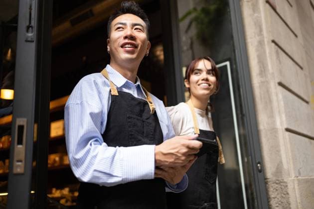 Creative Highlights Symbolfotos Cheerful employees of a chocolate store, wearing aprons, standing at the entrance, greeting customers with a welcoming smile Model Released DavidMunoz_ID24596_713026_033 Copyright: xDavidxMunozx RECORD DATE NOT STATED