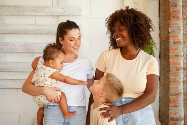 IMAGO Creative, Diversity, Familie: Gleichgeschlechtliche Eltern: Zwei Mütter A multiracial lesbian family shares a joyful moment together. The Caucasian and African American mothers are smiling and interacting with their children. The boy is looking up at his mother, while the toddler interacts with him Model Released HaruUraraStudio_ID24143_699789_047 Copyright: xHaruxUraraxStudiox RECORD DATE NOT STATED