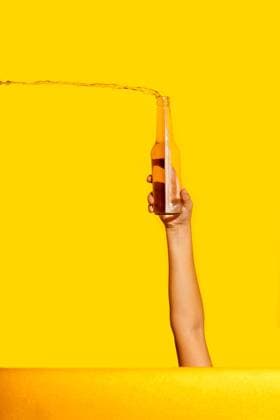 Creative Highlights Symbolfotos A creative image featuring a hand holding a glass bottle from which a clear beer is splashing out, all set against a vibrant yellow background Model Released SergioVictorVega_ID24526_711169_027 Copyright: xSergioxVictorxVegax RECORD DATE NOT STATED