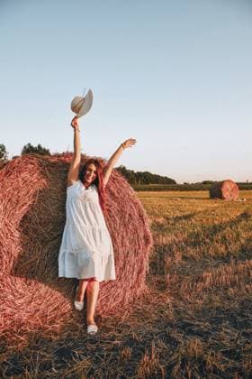Porträt der jungen glücklichen Frau fliegenden Hut auf dem Heuhaufen im Morgensonnenlicht, Landschaft. Schöne Frau in einem Kleid sitzt auf einem Heuhaufen. Cottagecore. Entspannen auf Sommerfeld mit Heuhaufen. Frische Luft auf dem Land. pastorales Leben Portrait of young happy woman flying hat on the haystack in morning sunlight, countryside. Beautiful woman in a dress sits on a haystack. Cottagecore. relaxing on summer field with hay stacks. Fresh air contryside. pastoral life Copyright: imageBROKER AnastasiiaxYanishevs ibxiqx11313126.jpg ,model released, Symbolfoto ,property released
