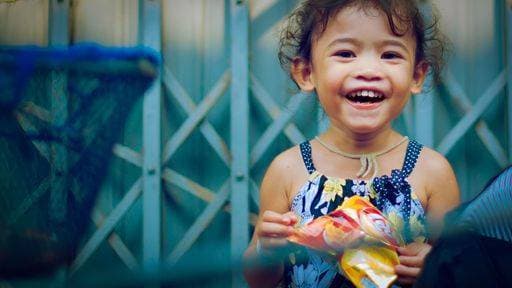 Creative Highlights Symbolfotos A joyful young girl in a floral dress holding a snack, smiling brightly in front of a metal gate. 25767616 ,model released, Symbolfoto RECORD DATE NOT STATED