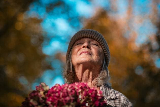 Portrait of a beautiful senior woman standing outdoors with her eyes closed. Autumn nature behind her. Portrait of beautiful senior woman standing outdoors with her eyes closed. Autumn nature behind her. model released