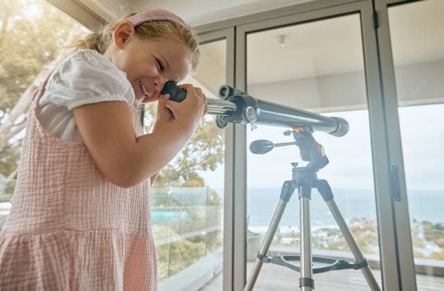 Young kids, telescope and home learning about planets, stars and sky in space. Excited, curious and happy girl play, watch and study view of universe, science and moon for fun educational development. model released property released Copyright: xwww.peopleimages.comx