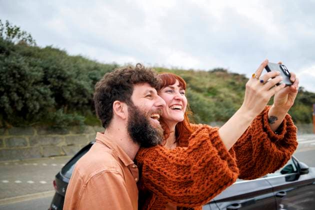 Creative Highlights Symbolbilder Joyful couple taking a selfie outdoors with a digital camera, both smiling broadly with a road and greenery in the background. bola04762 Copyright: xConnectxImagesx ,model released