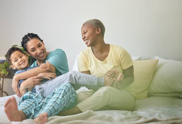 IMAGO Creative, Diversity, Familie: Gleichgeschlechtliche Eltern: Zwei Mütter Morning, gay family and hug on bed in home bedroom for security, quality time and love. Adoption, lesbian or LGBTQ women or parents and a happy foster kid together to wake up with care and fun play. model released property released Copyright: xwww.peopleimages.comx